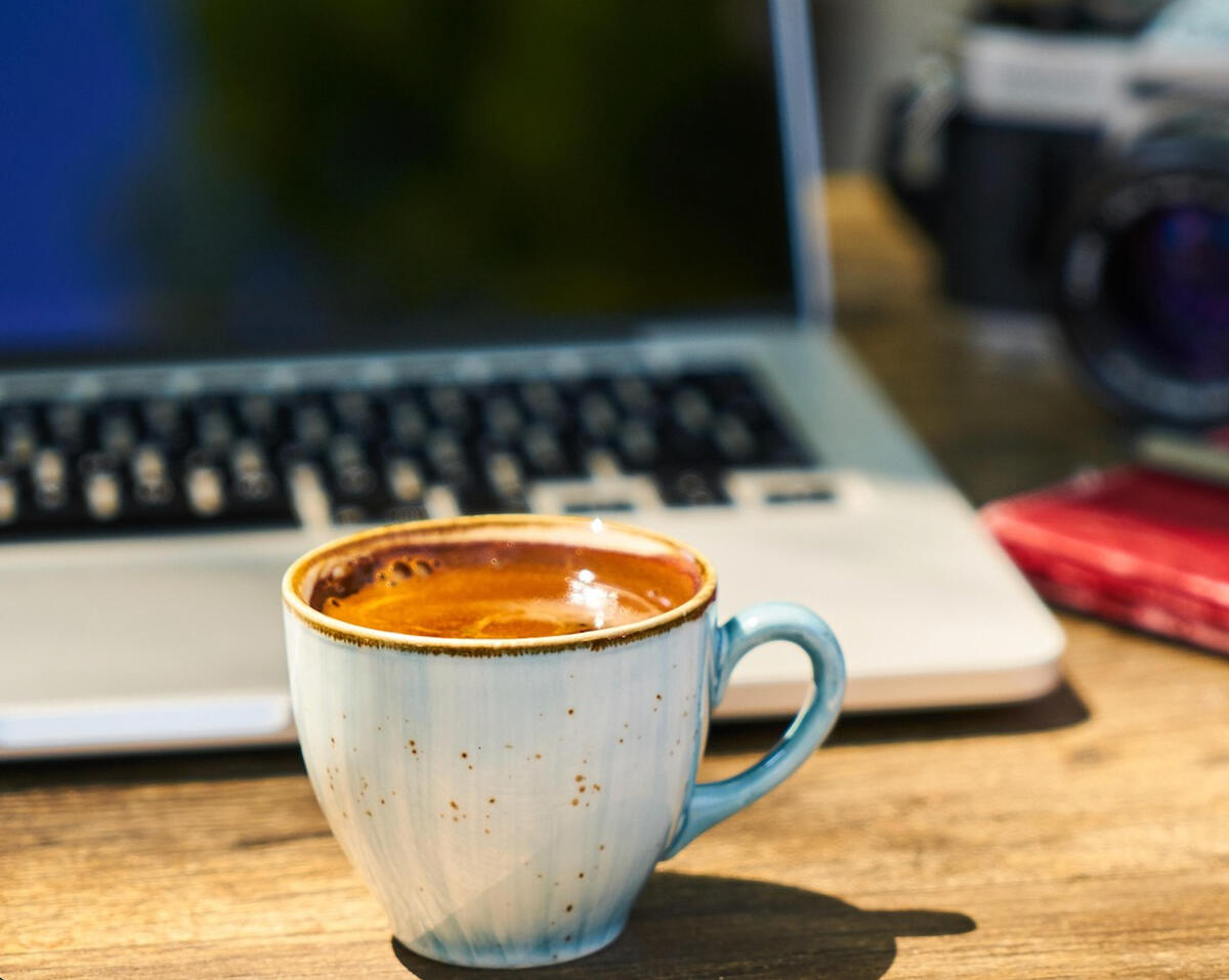 Online therapy in Ontario with Kelly (MSW, RSW). A sunny wooden desk with a laptop, therapy journal, and hot coffee.
